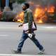 A man carries looted items from a store as police vehicles burn.